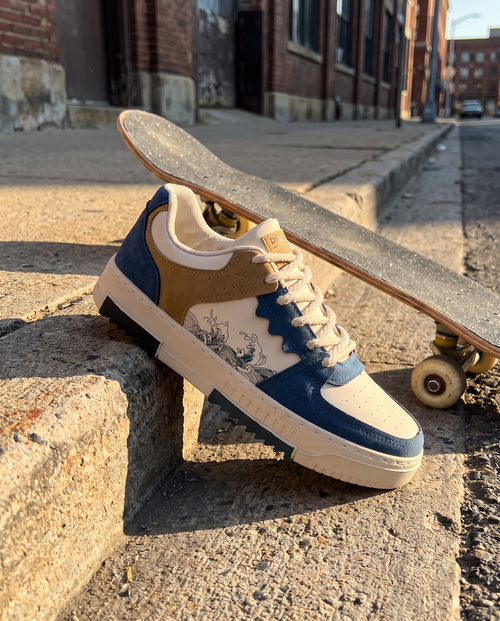 Men's blue lace-up fashion sneaker on an urban sidewalk edge with a skateboard